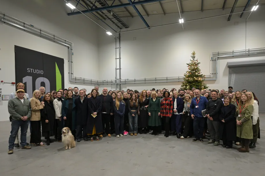The Queen smiles with cast and crew during a visit to the Rivals set